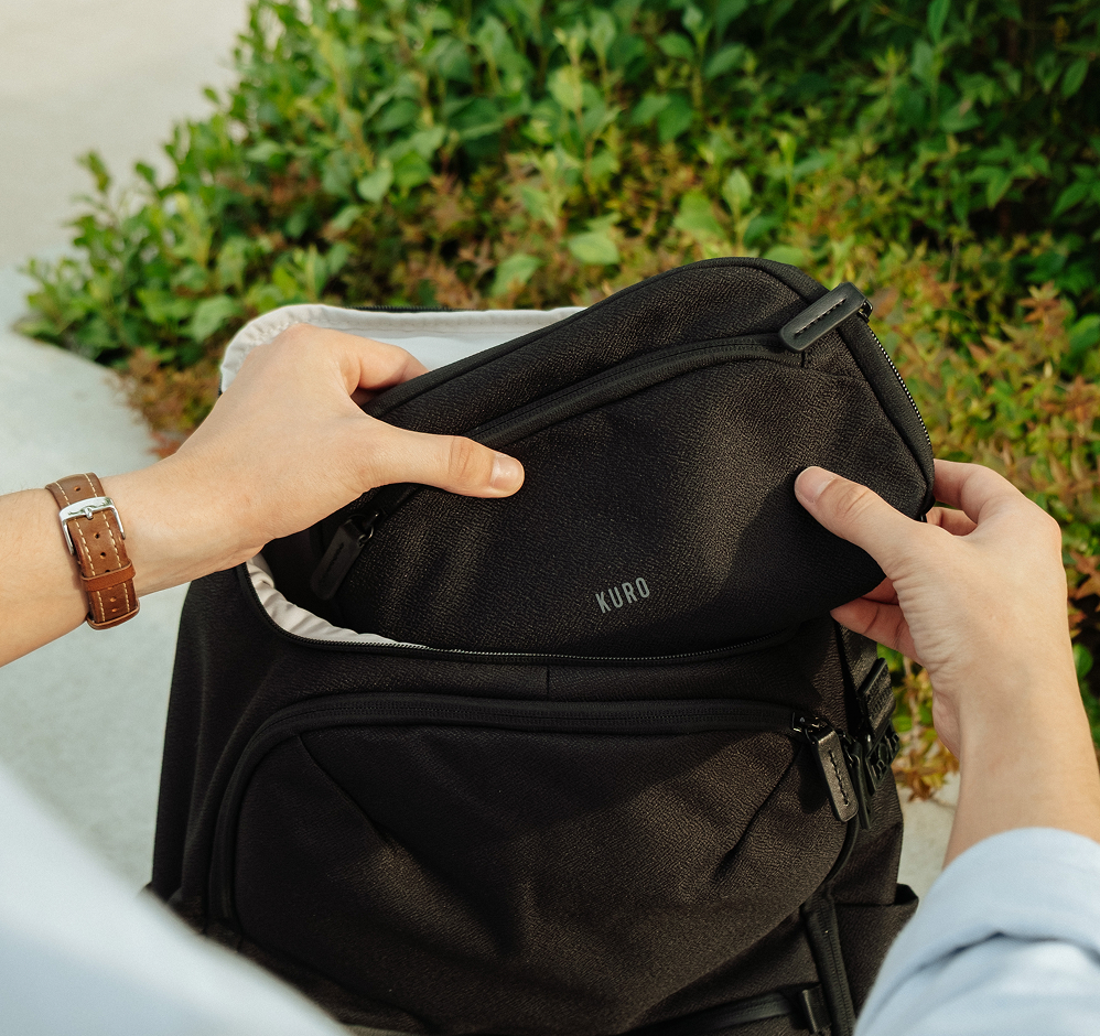 Close-up of hands detaching the Kuro essentials bag from the main backpack outdoors